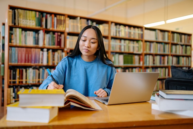 Woman studying in a library with books and a laptop
