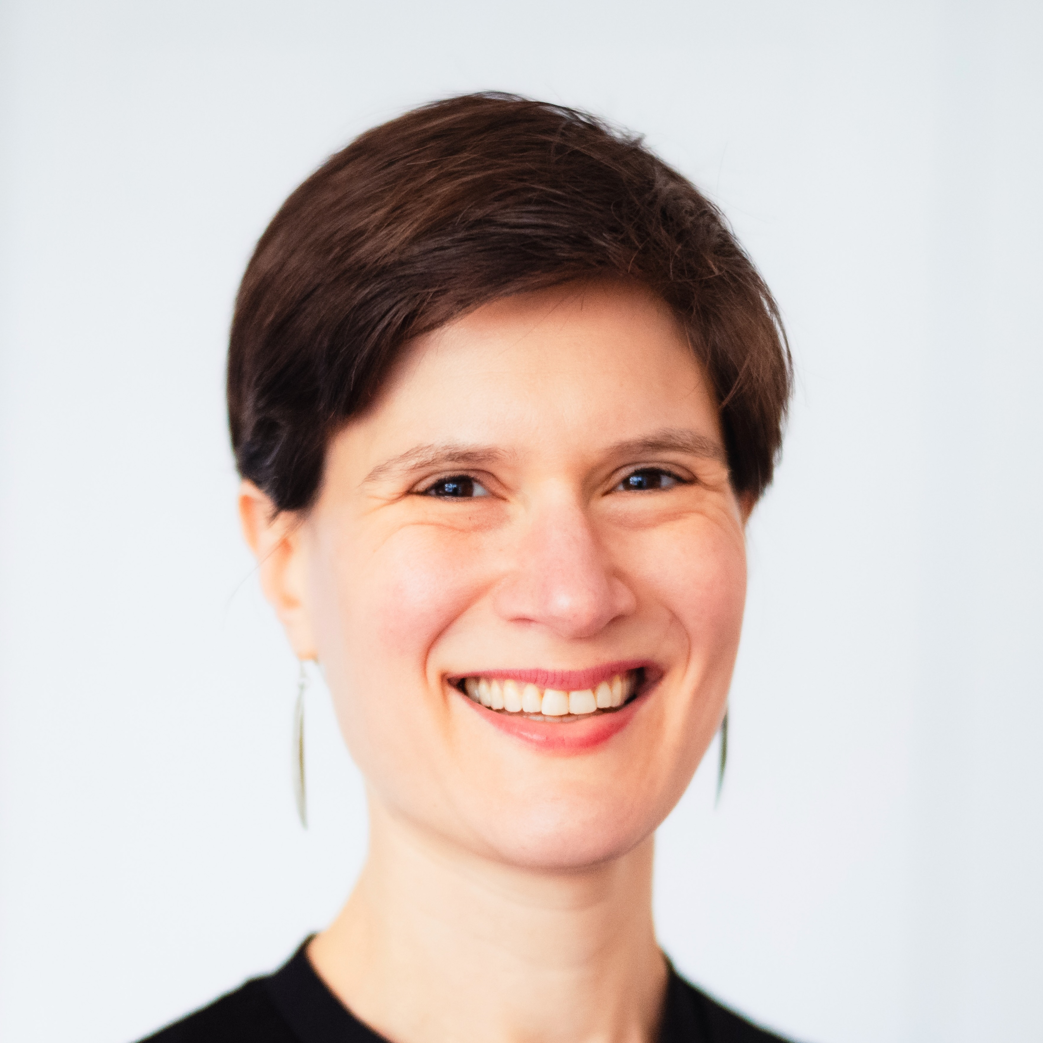 Headshot of Ella against a white background, smiling. She is a white woman in her 40s with short dark hair.